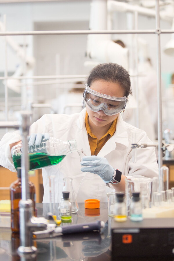 Female chemistry student pouring green liquid into small beaker
