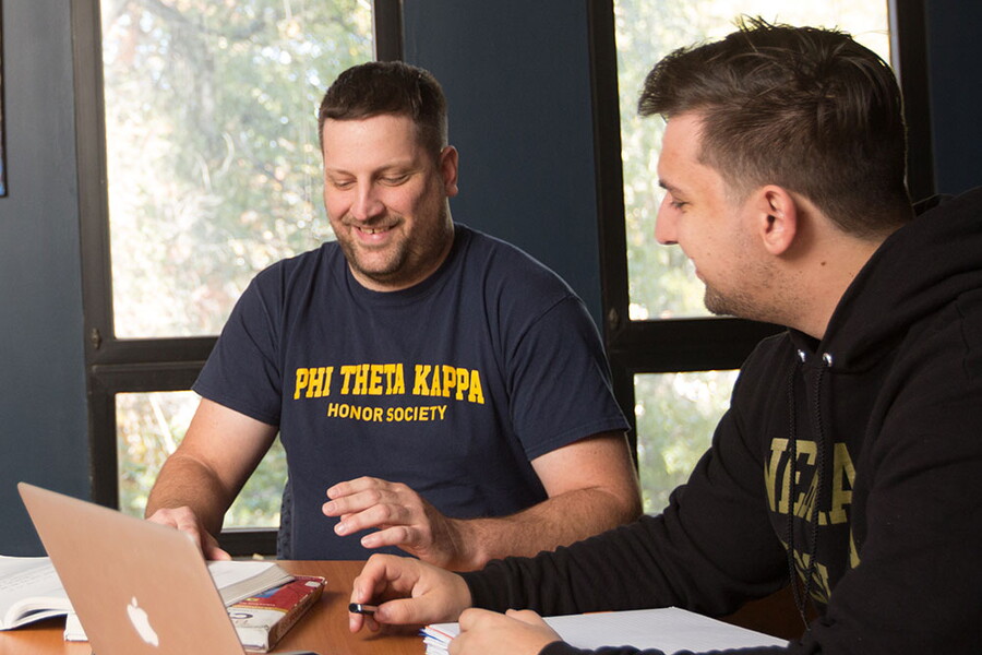 Two male students at a conference table. One students sweatshirt reads Phi Theta Kappa Honors Society.